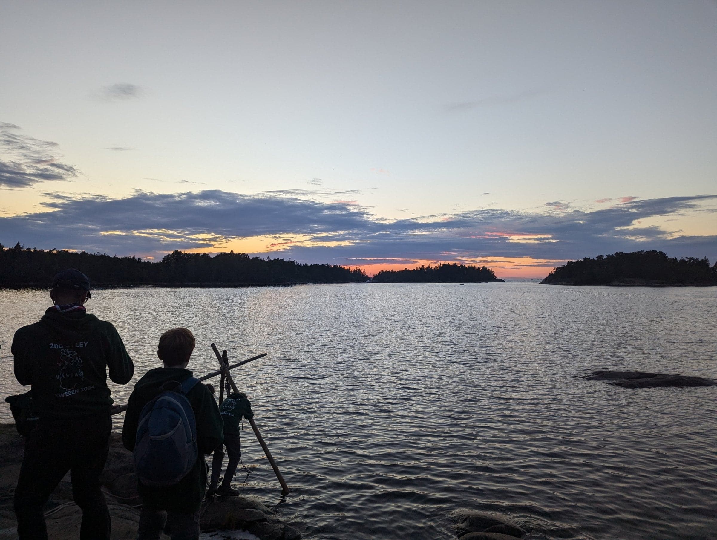 Scouts building a lever to raise blocks from the water while the sun sets, in Vassaro, Sweden